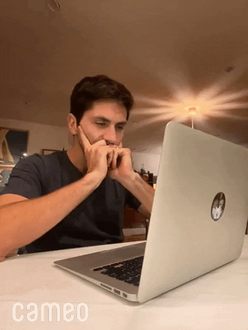A confused man sits at a desk, looking overwhelmed by work on a laptop.